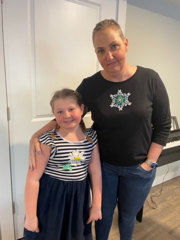 Woman with shaved head stands next to young daughter.