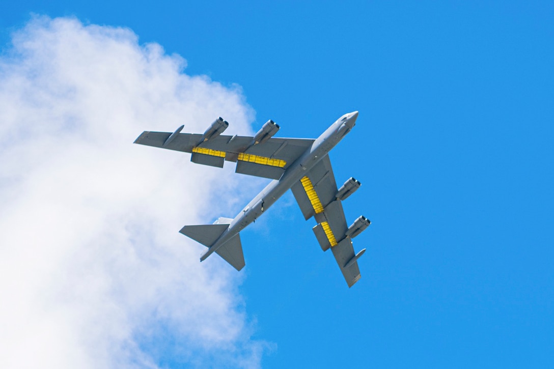 An aircraft flies at an angle next to a cloud as seen from below.