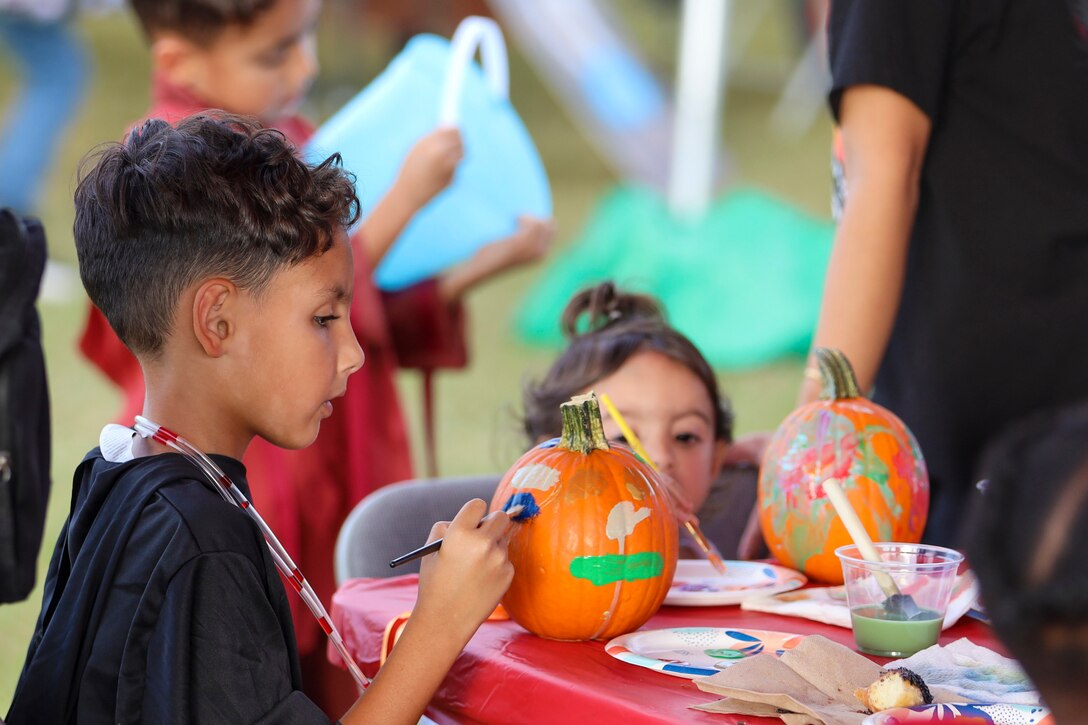 Children sit at a table and paint pumpkins.