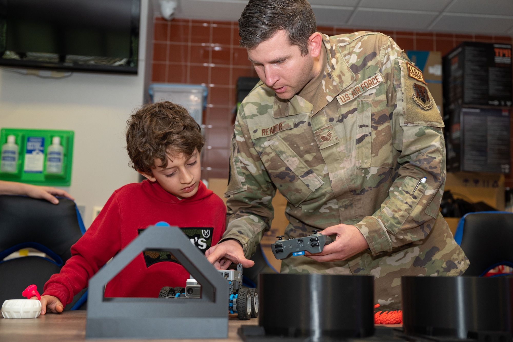 A man holding a controller points to a robot on a table in front of a boy.