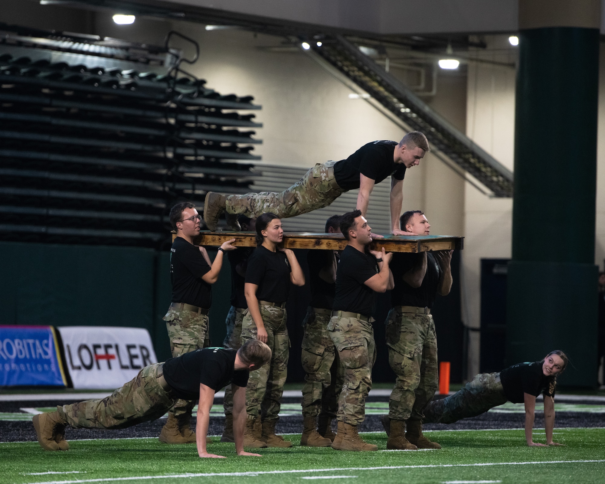 Military members stand holding a board with a servicemember on it.