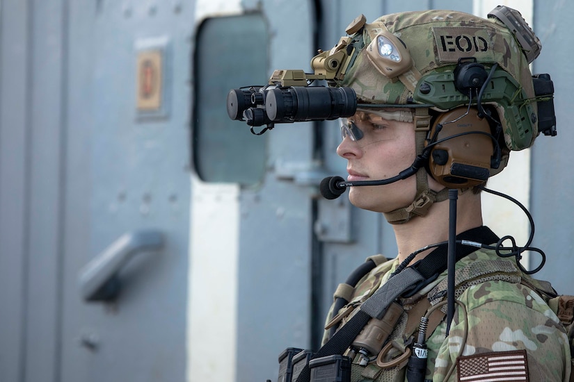 A sailor wearing a helmet with a patch that reads "EOD" looks into the distance.