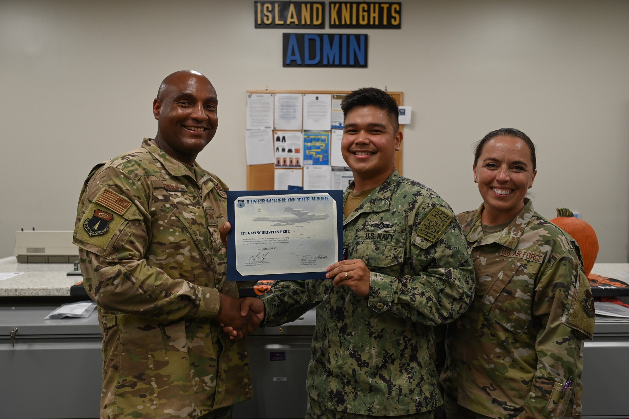 Two Airmen and a Sailor pose for a photo while the sailor holds a certificate.