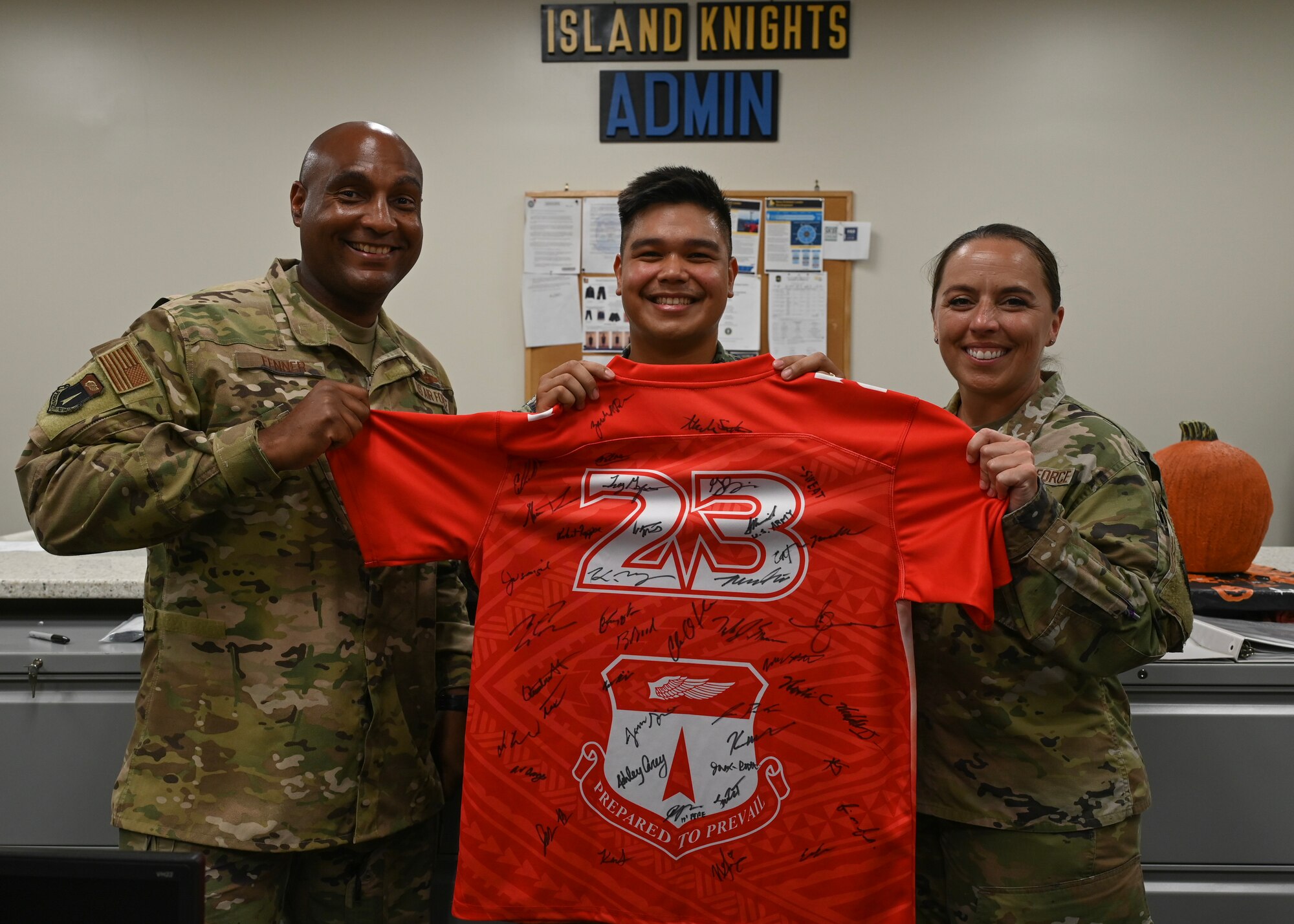 Two Airmen and a Sailor pose for a photo while holding a jersey together.