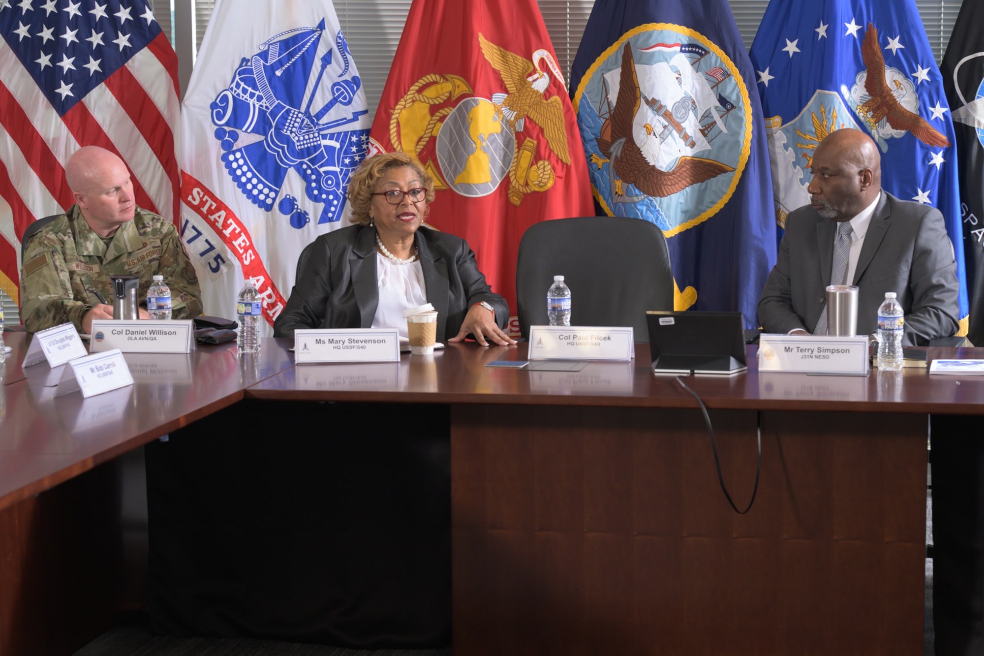 Three people seated at a conference table have a conversation.