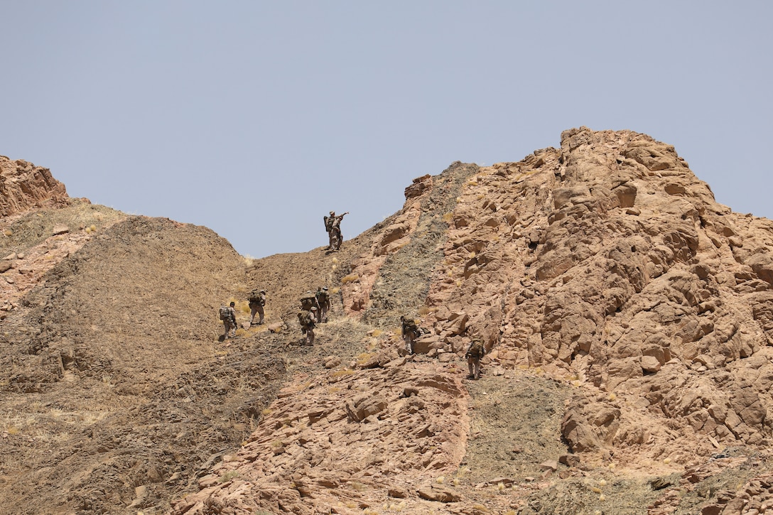 Marines climb up an arid, rocky hill.