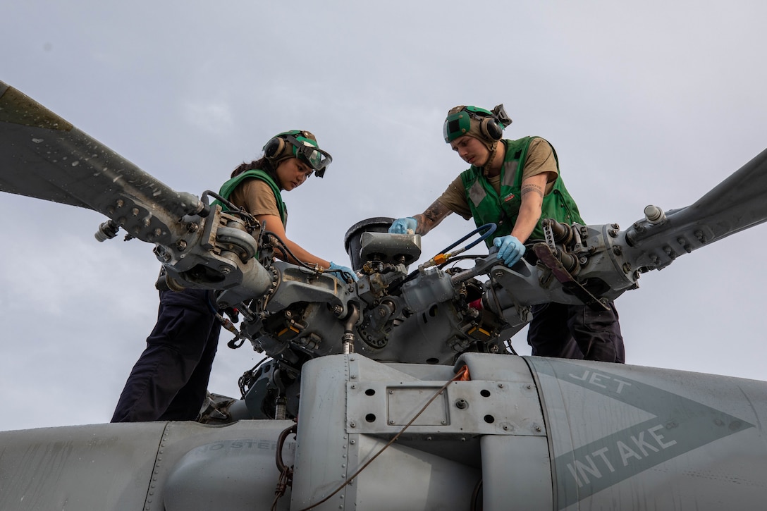 Two  service members clean a helicopter at sea.