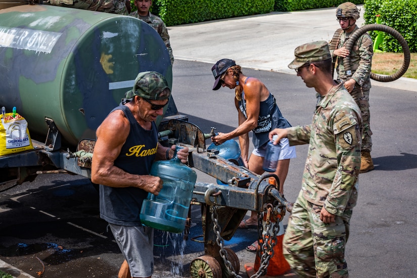 A man and woman in civilian clothes fill water jugs from a military water distribution tank.