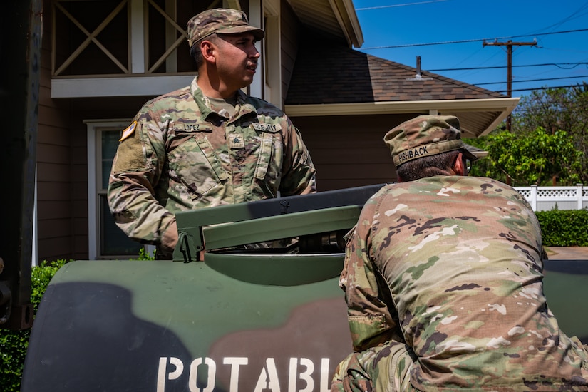 Service members stand near a military water distribution tank.