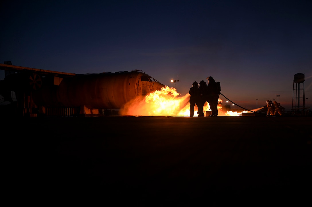 Airmen spray water hoses on a fire during training at night.