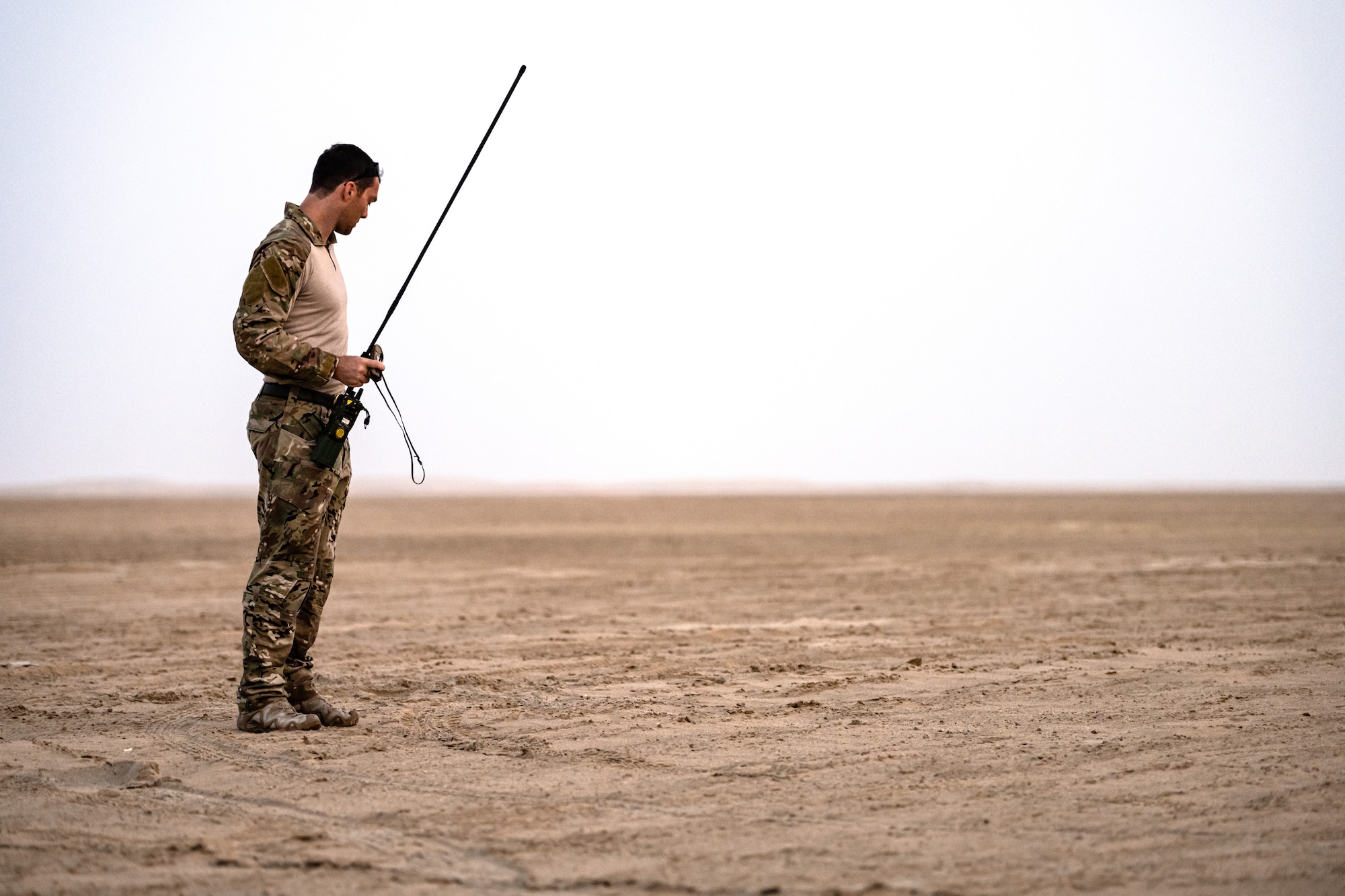 Military member holding a radio in the desert