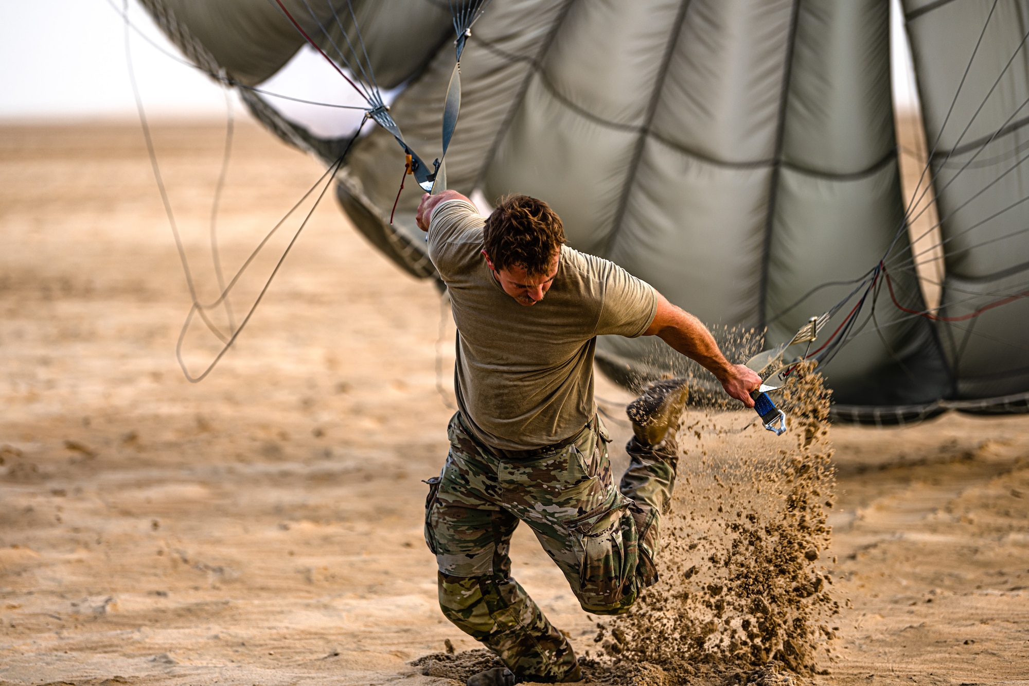 Military member kicking sand up while dragging a parachute through the desert