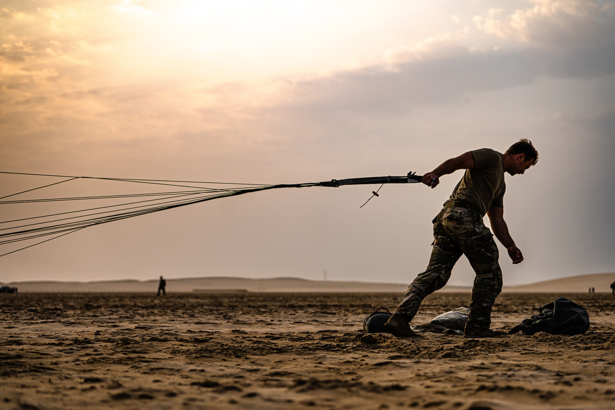 Military member dragging a parachute through the sand