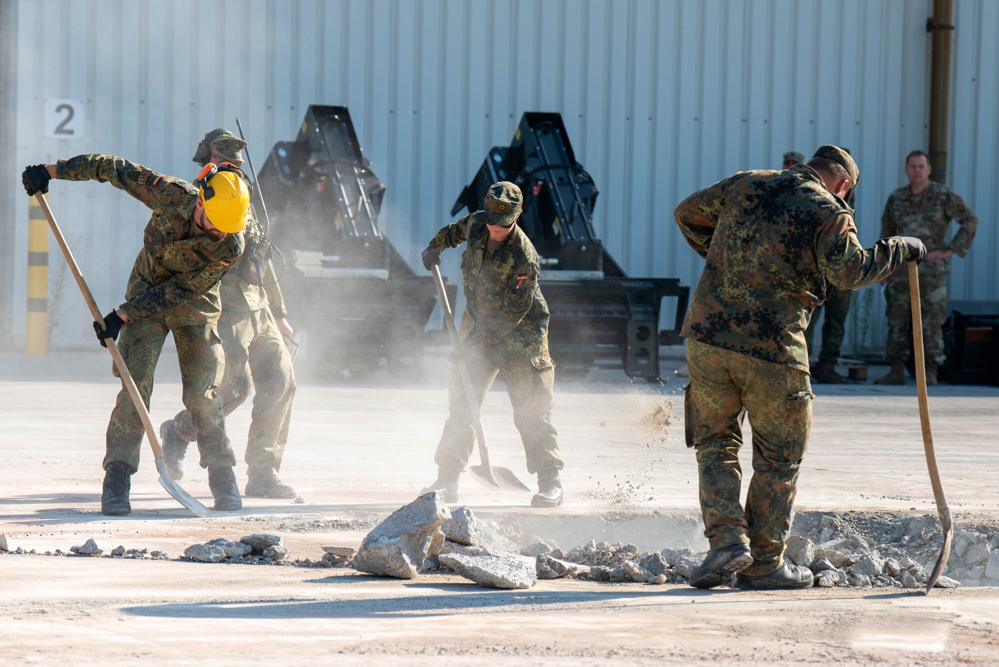 German air force members sweep debris into simulated airfield damage during an airfield repair demonstration