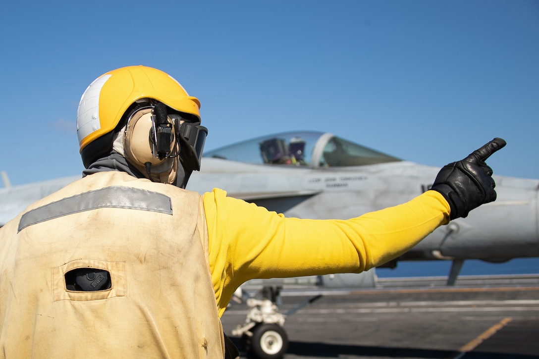 A sailor gives signals to an F/A-18E.