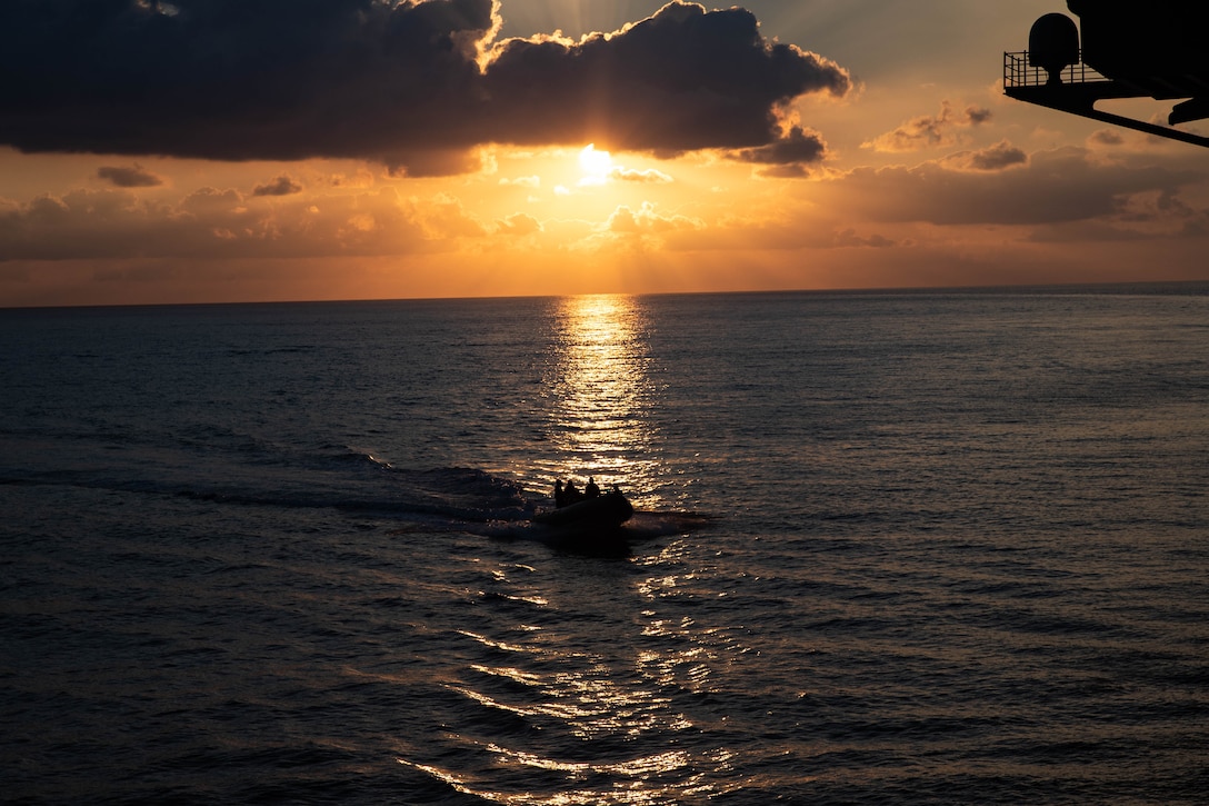 Sailors conduct small-boat operations in a rigid-hull inflatable boat at twilight.