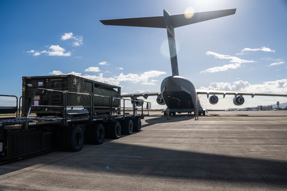 A vehicle carries cargo to load in the back of a large aircraft.