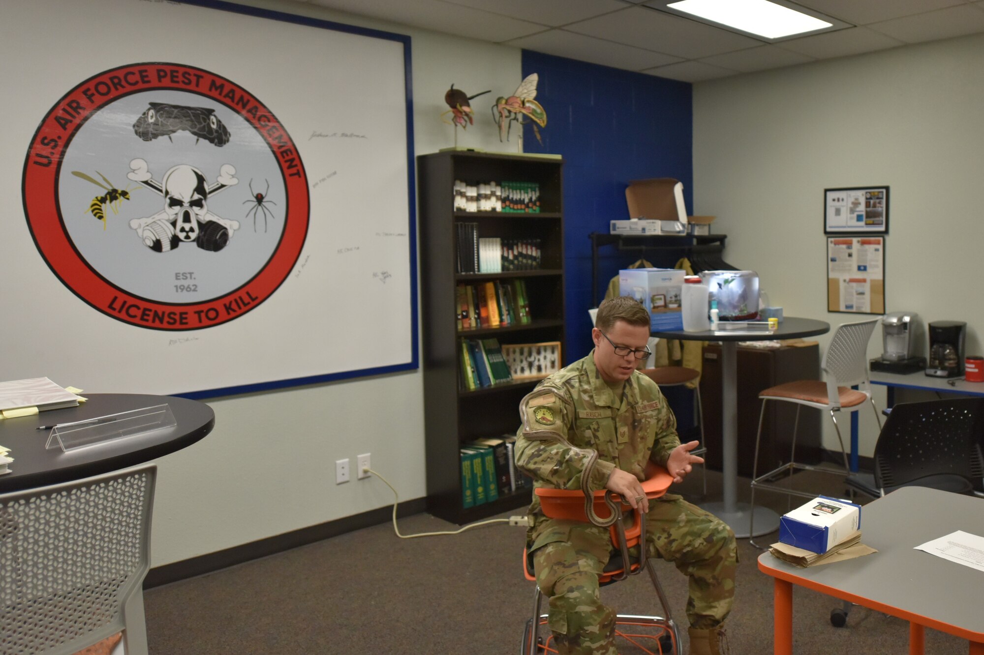 An Airman sits in a seat that allows multiple seating positions for increased student comfort and attention. He is holding a snake.