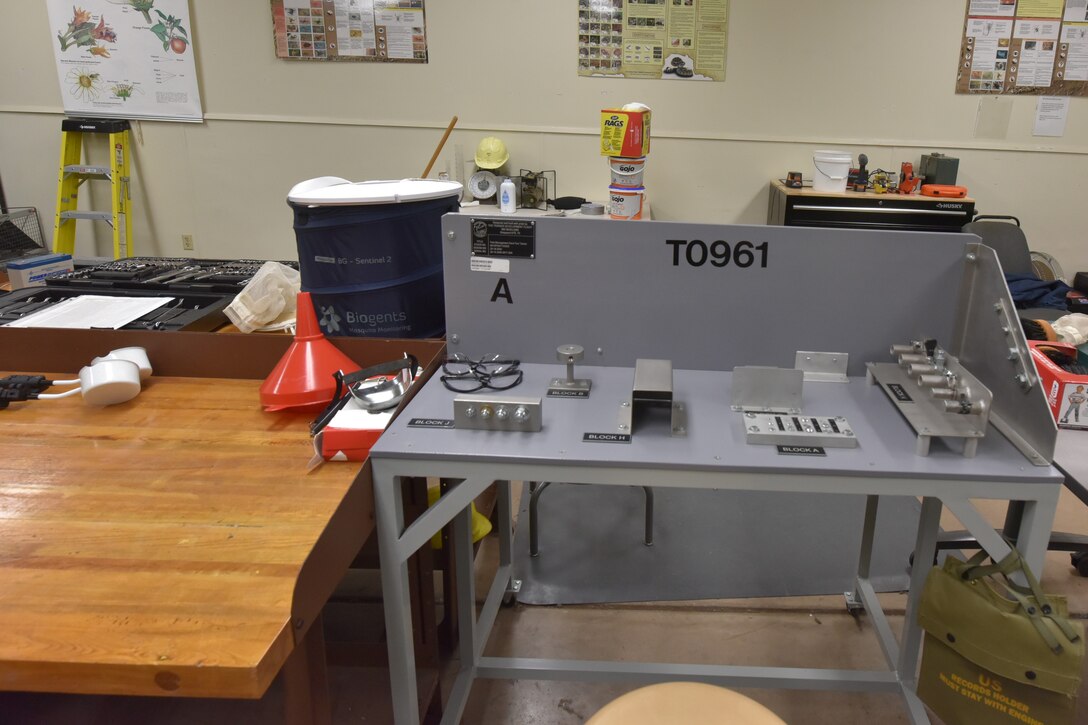 A gray table with nuts and bolts attached used to train students to use tools