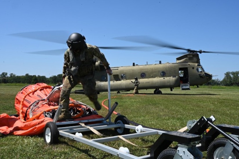 A service member works in front of a helicopter in a field.