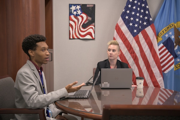 Two employees sit at a table to take part in a group meeting.
