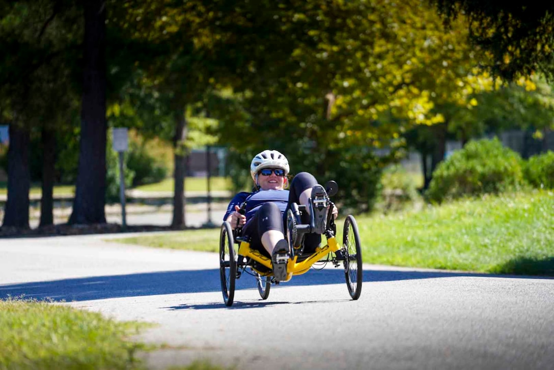 A retired sailor rides a recumbent bike down a sidewalk.