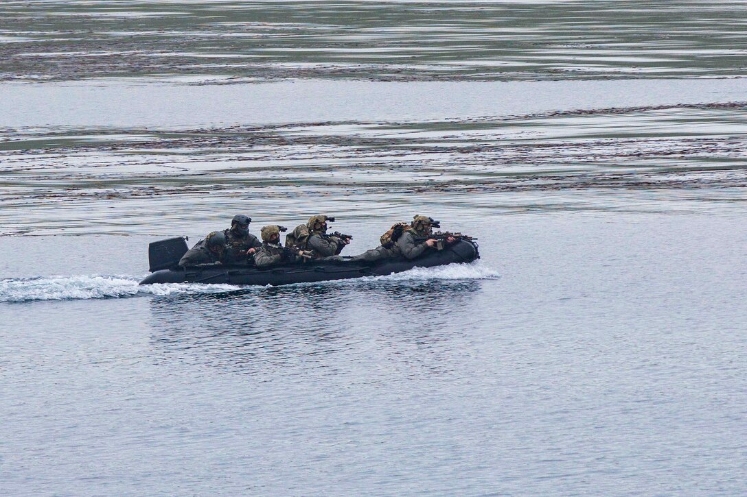 Sailors move through a body of water in an inflatable boat with weapons drawn.