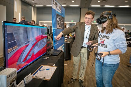 Micaela Rapp, mechanic helper trainee, Shop 52, Regional Calibration, tests a custom learning program with the help of chief innovation officer David Oyanadel, of Arsome Technology Sept. 14, 2022 during the annual PSNS & IMF Technology Showcase at the Kitsap Conference Center in Bremerton, Washington. (U.S. Navy photo by Scott Hansen)