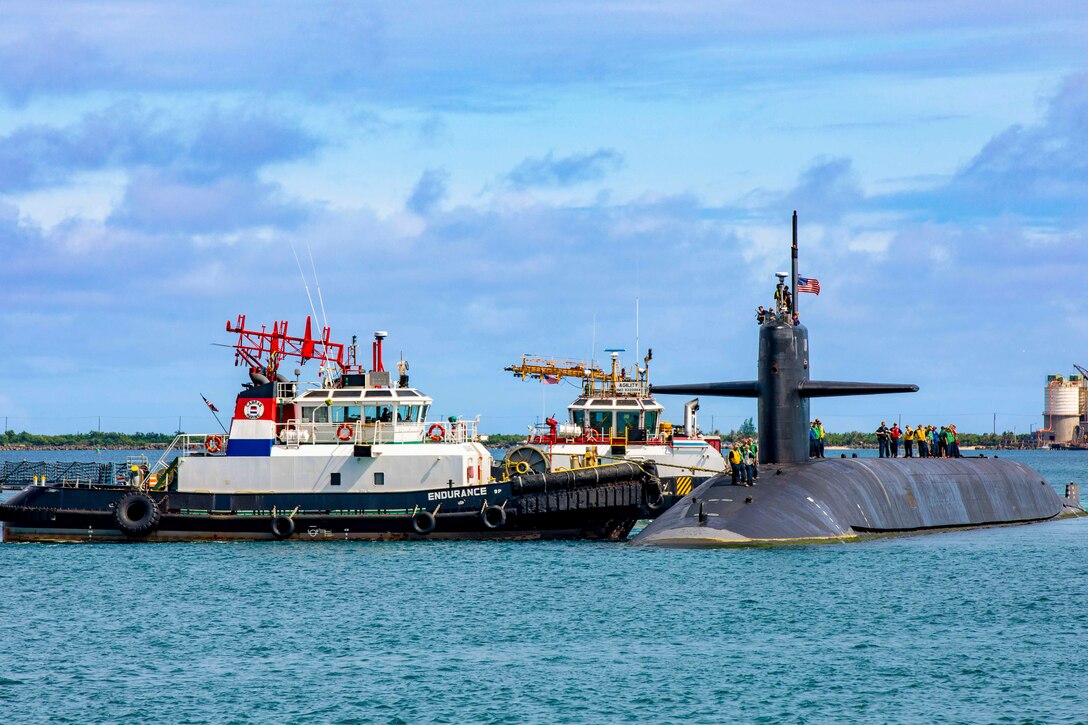 Two boats park next to a submarine with sailors working on top in colorful jerseys in a body of water.