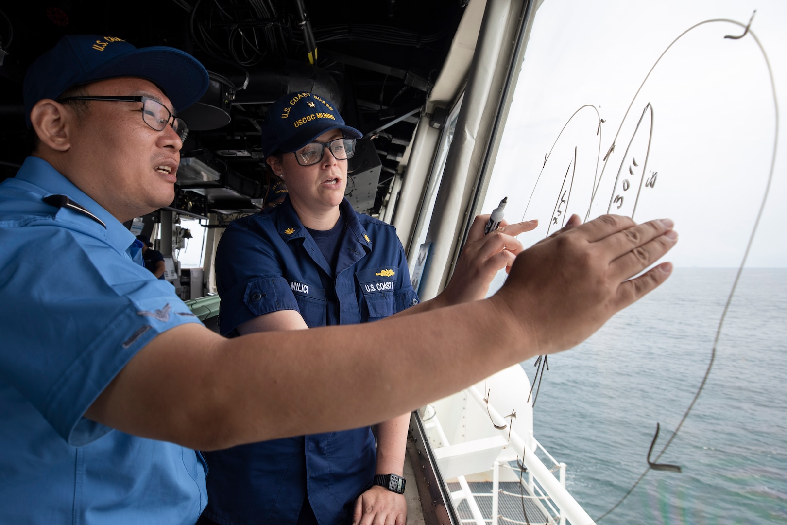 Assistant Inspector Lim SiYong (left) and Lt. Cmdr. Lauren Milici plan out small-boat maneuvers on the bridge of U.S. Coast Guard Cutter Munro (WMSL 755) during an at-sea engagement with Korea Coast Guard vessel KCG 3011 (Badaro) in the Tsushima Strait Aug. 16, 2023. Munro is deployed to the Indo-Pacific to advance relationships with ally and partner nations to build a more stable, free, open, and resilient region with unrestricted, lawful access to the maritime commons. (U.S. Navy photo by Chief Petty Officer Brett Cote)