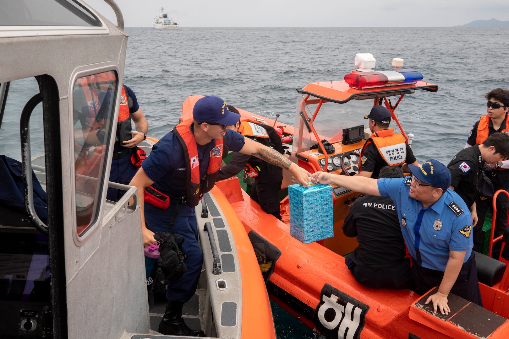 Assistant Inspector Lim SiYong (right) passes a gift to Petty Officer 2nd Class Samuel Zarraonandia at the conclusion of an at-sea engagement between U.S. Coast Guard Cutter Munro (WMSL 755) and Korea Coast Guard vessel KCG 3011 (Badaro) in the Tsushima Strait Aug. 16, 2023. Munro is deployed to the Indo-Pacific to advance relationships with ally and partner nations to build a more stable, free, open, and resilient region with unrestricted, lawful access to the maritime commons. (U.S. Navy photo by Chief Petty Officer Brett Cote)