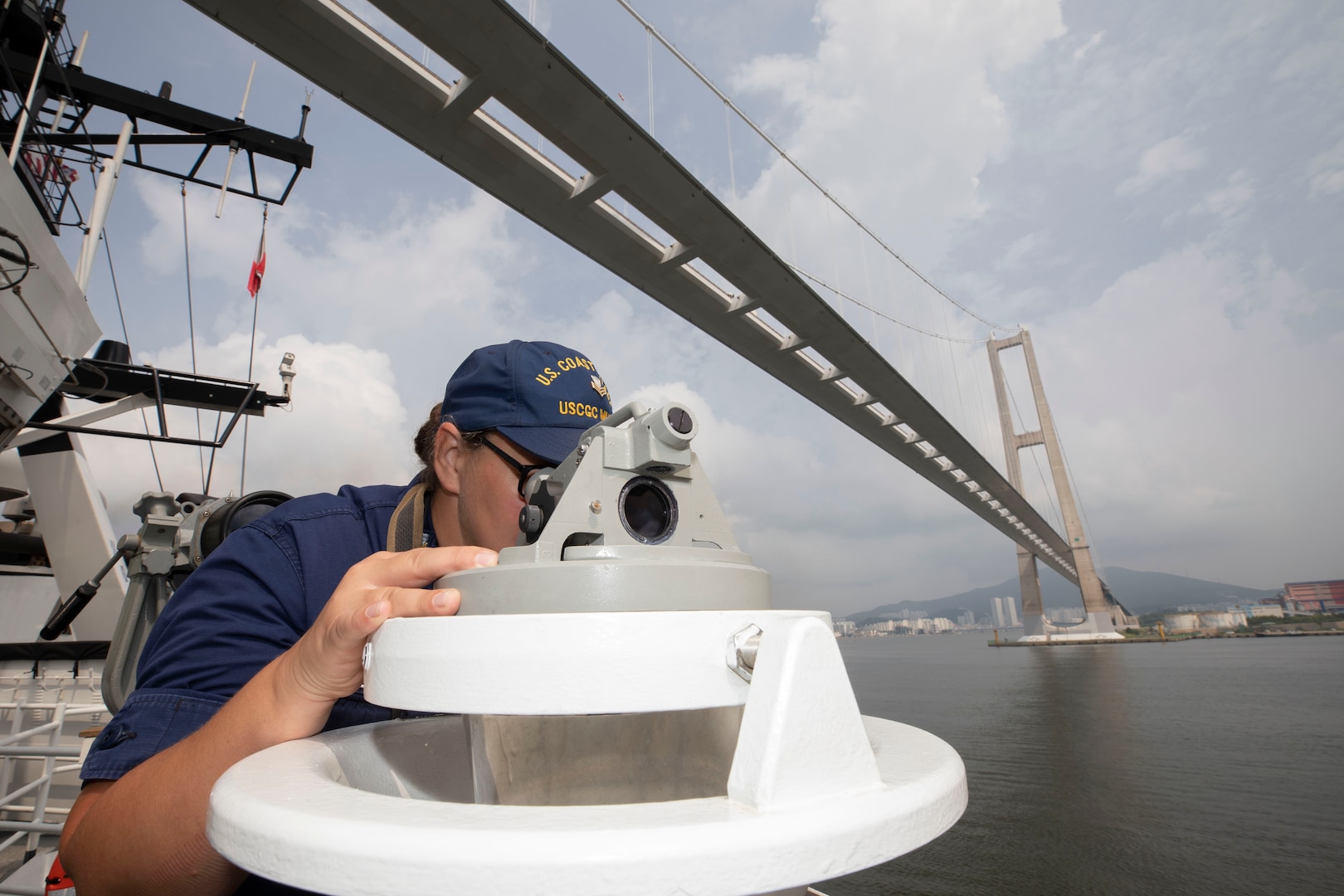 Petty Officer 1st Class Leslie Canazon uses an azimuth to shoot a bearing as U.S. Coast Guard Cutter Munro (WMSL 755) departs the Port of Gwangyang, Republic of Korea, to begin an at-sea engagement with the Korea Coast Guard Aug. 16, 2023. Munro is deployed to the Indo-Pacific to advance relationships with ally and partner nations to build a more stable, free, open, and resilient region with unrestricted, lawful access to the maritime commons. (U.S. Navy photo by Chief Petty Officer Brett Cote)