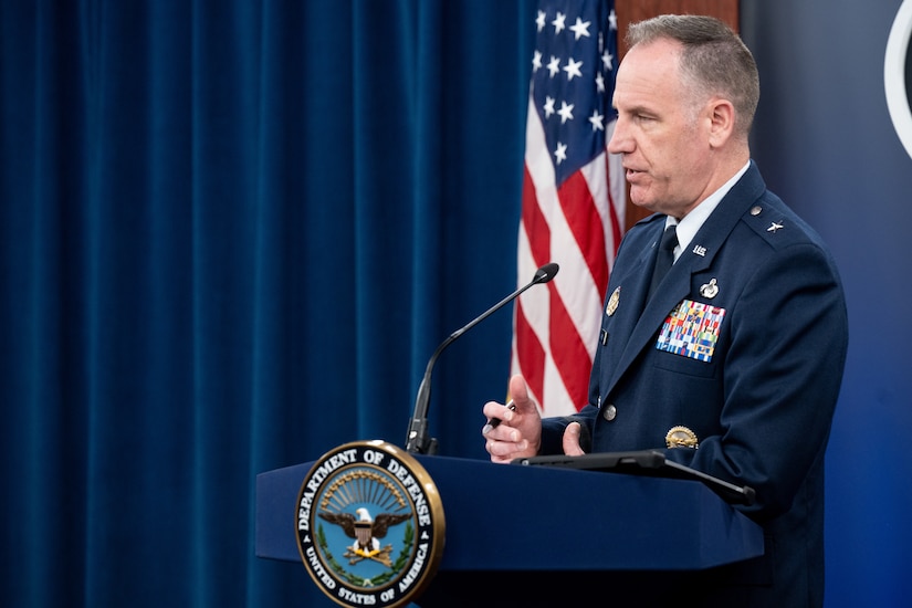 A man speaks from a podium in front of an American flag.