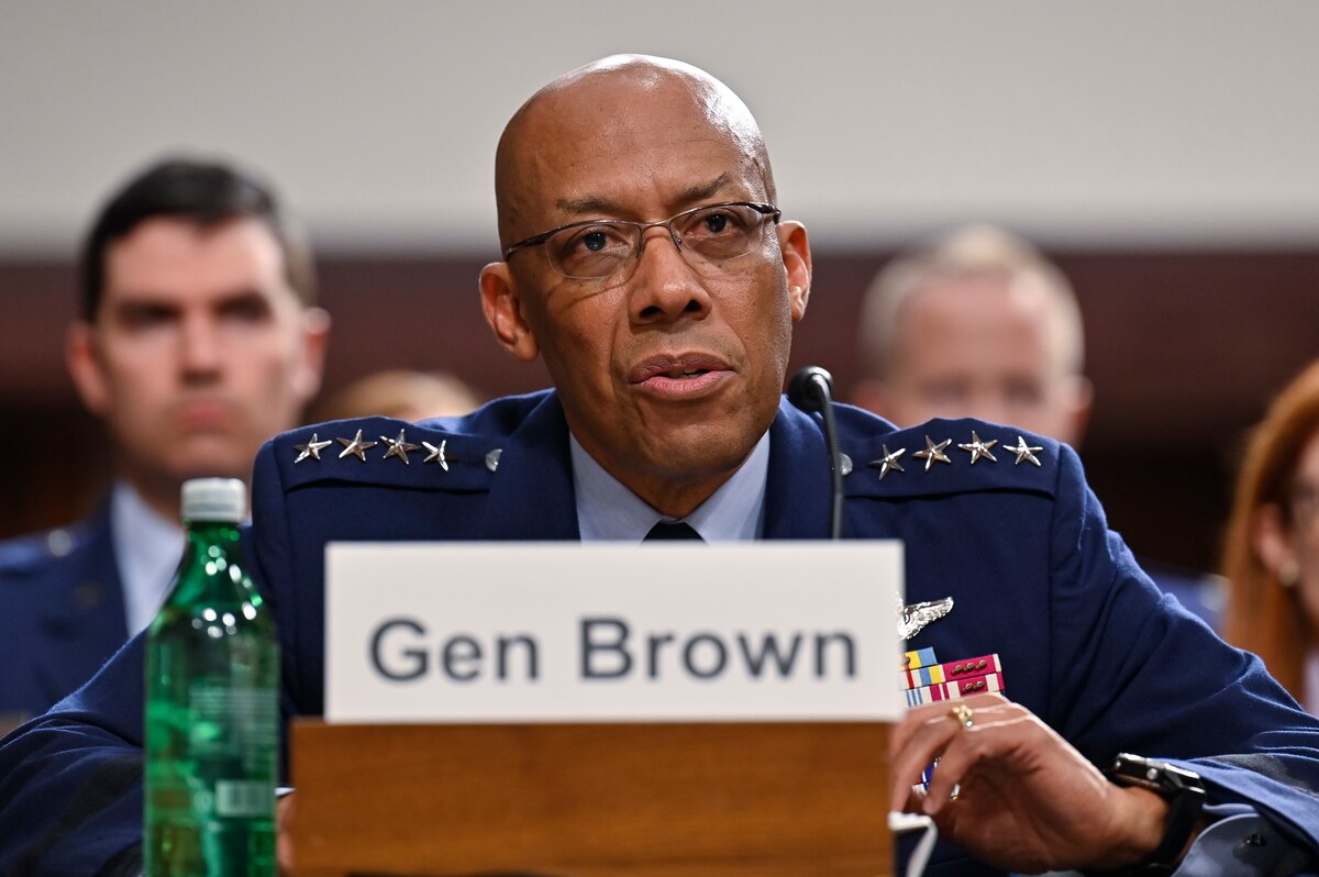 A man in a military uniform is seated at a table with a microphone.