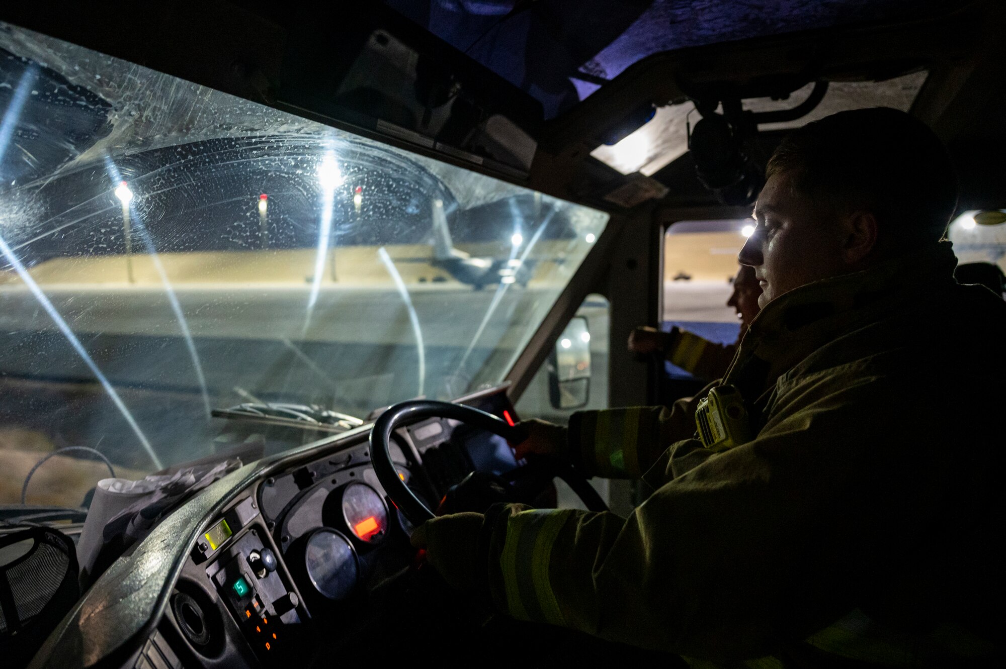 Military member in firefighter gear drives a firetruck towards a KC-135