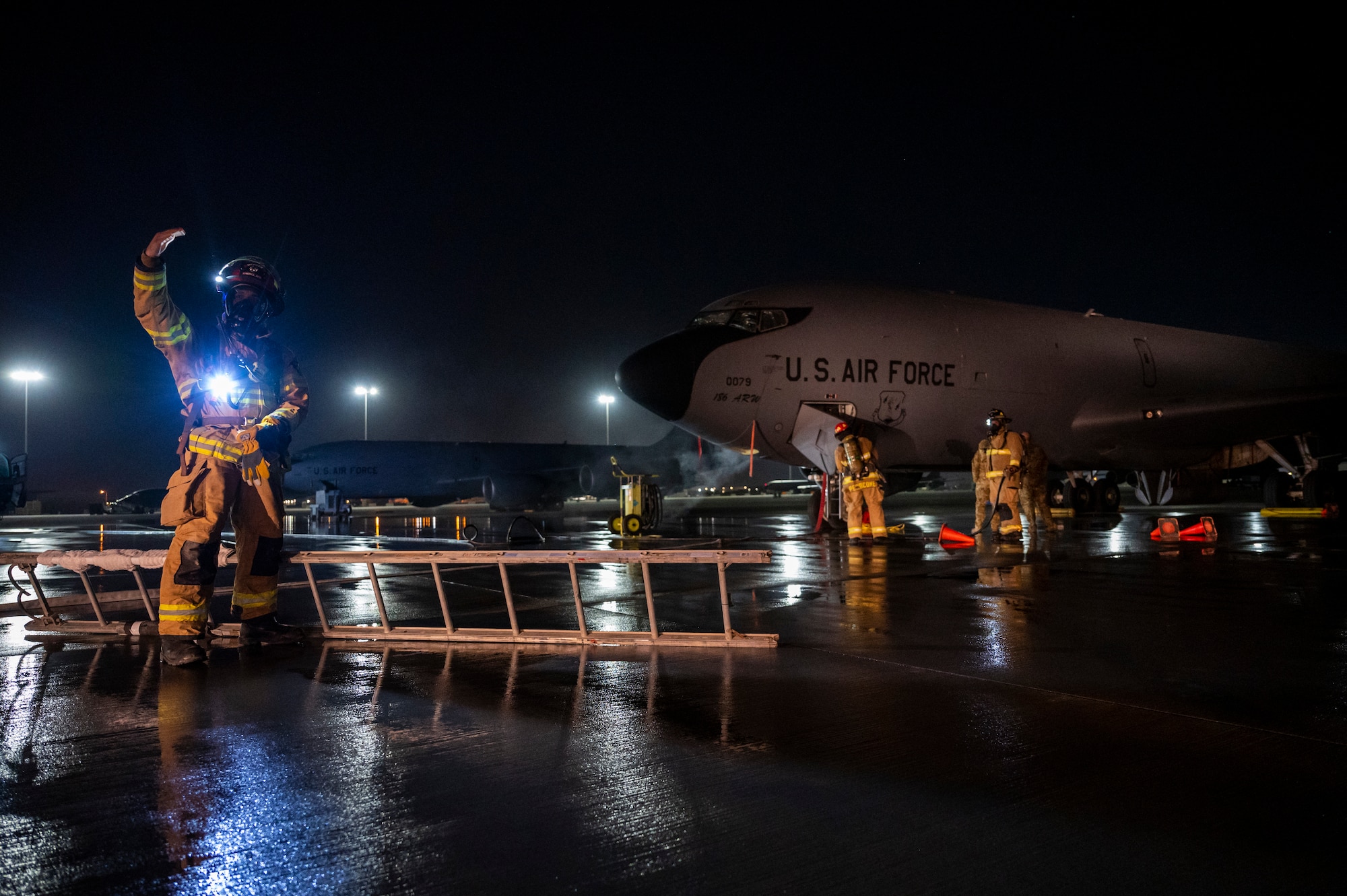 Military member in firefighter gear carries a ladder towards a KC-135