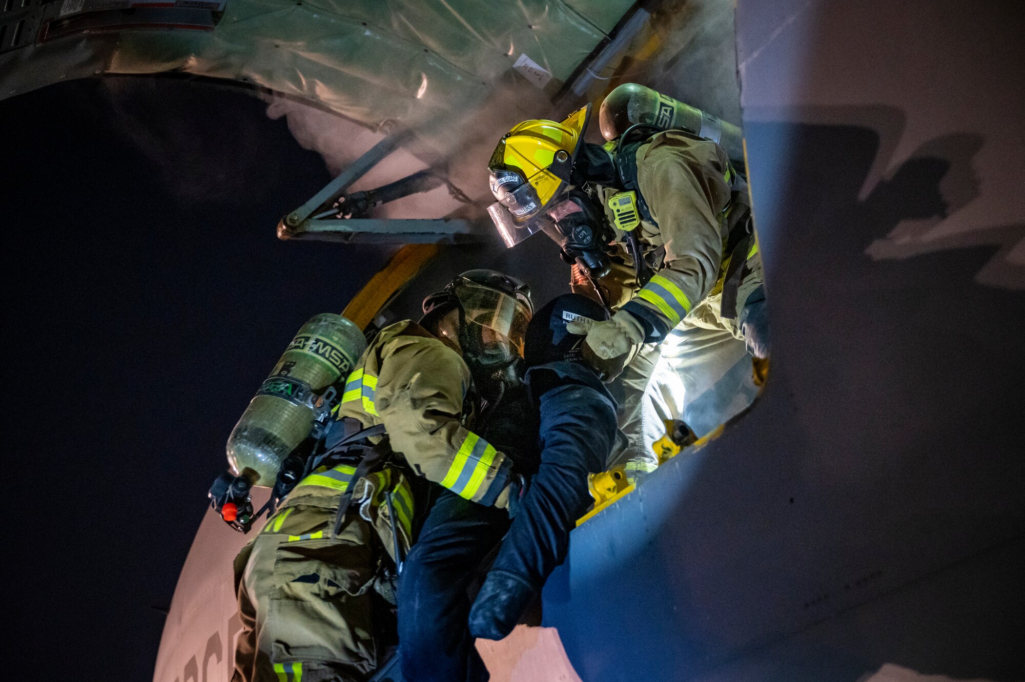 Military members in firefighter gear carry a mannequin out of a KC-135