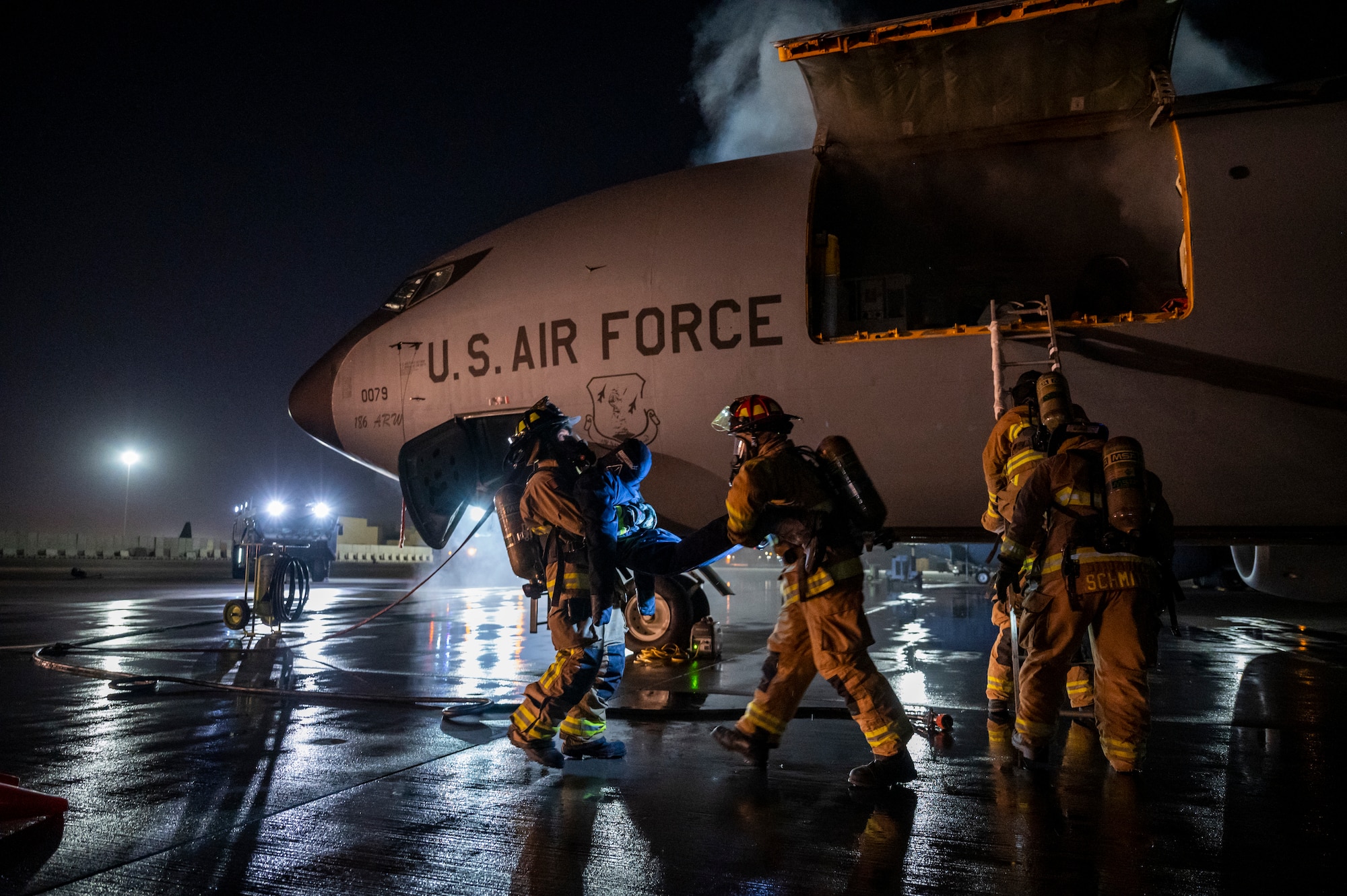 Military members in firefighter gear carry a mannequin out of a KC-135