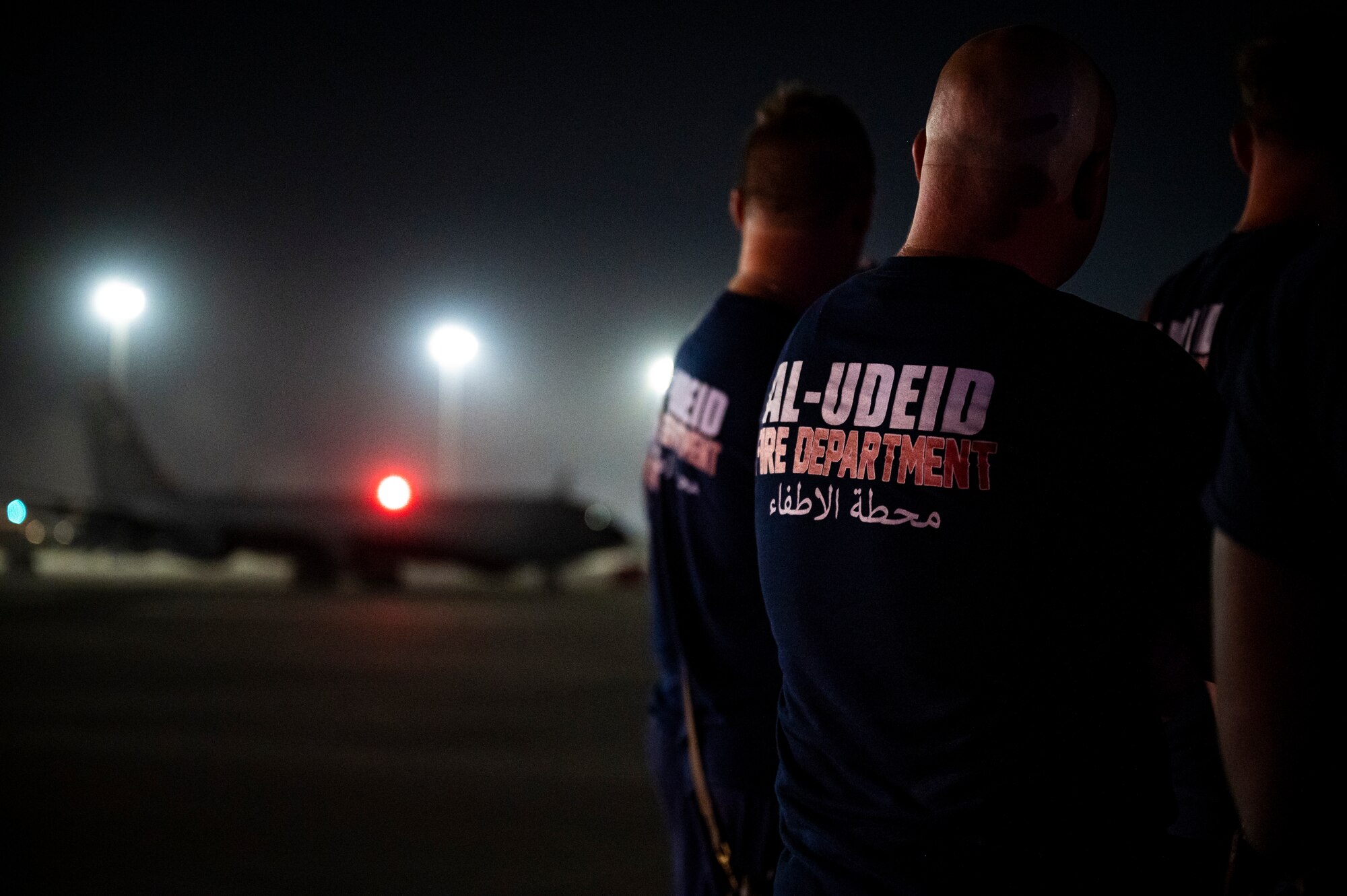 Military member wearing a shirt displaying "Al-Udeid Fire Department" stands in front of a KC-135