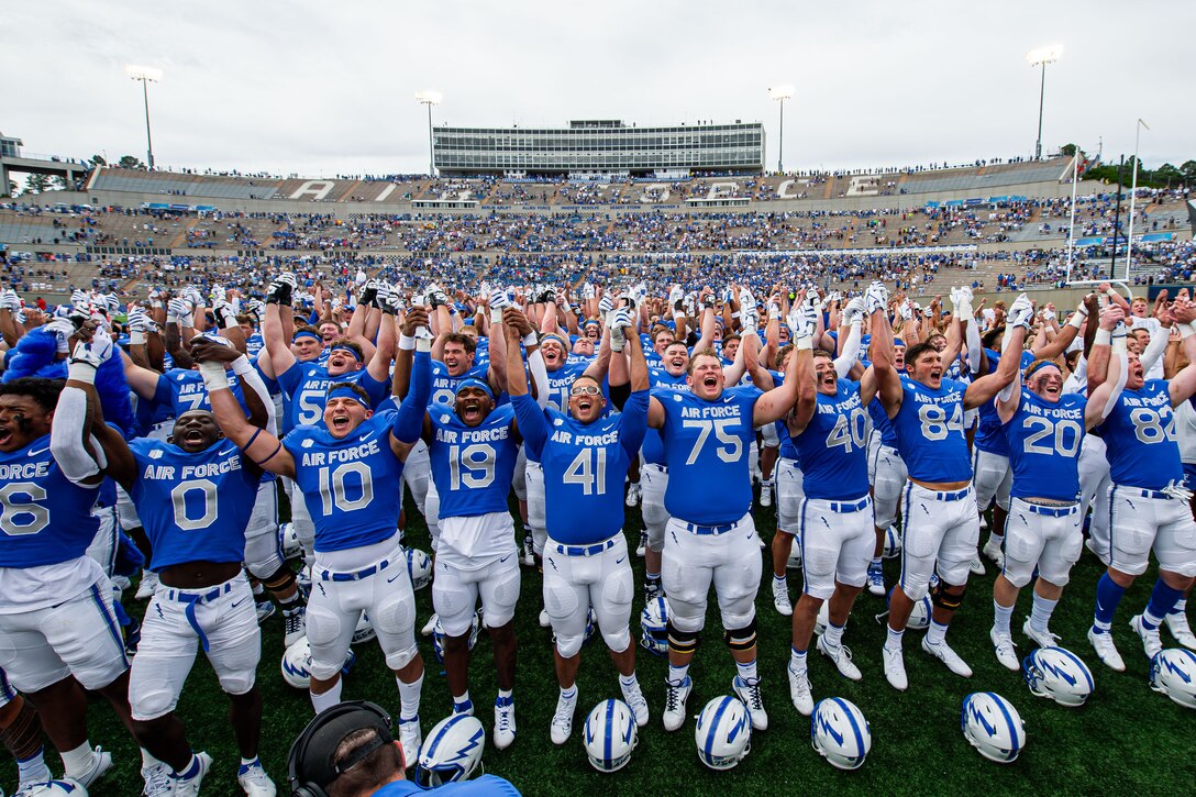 A team of football players cheer and put their hands together in a stadium.