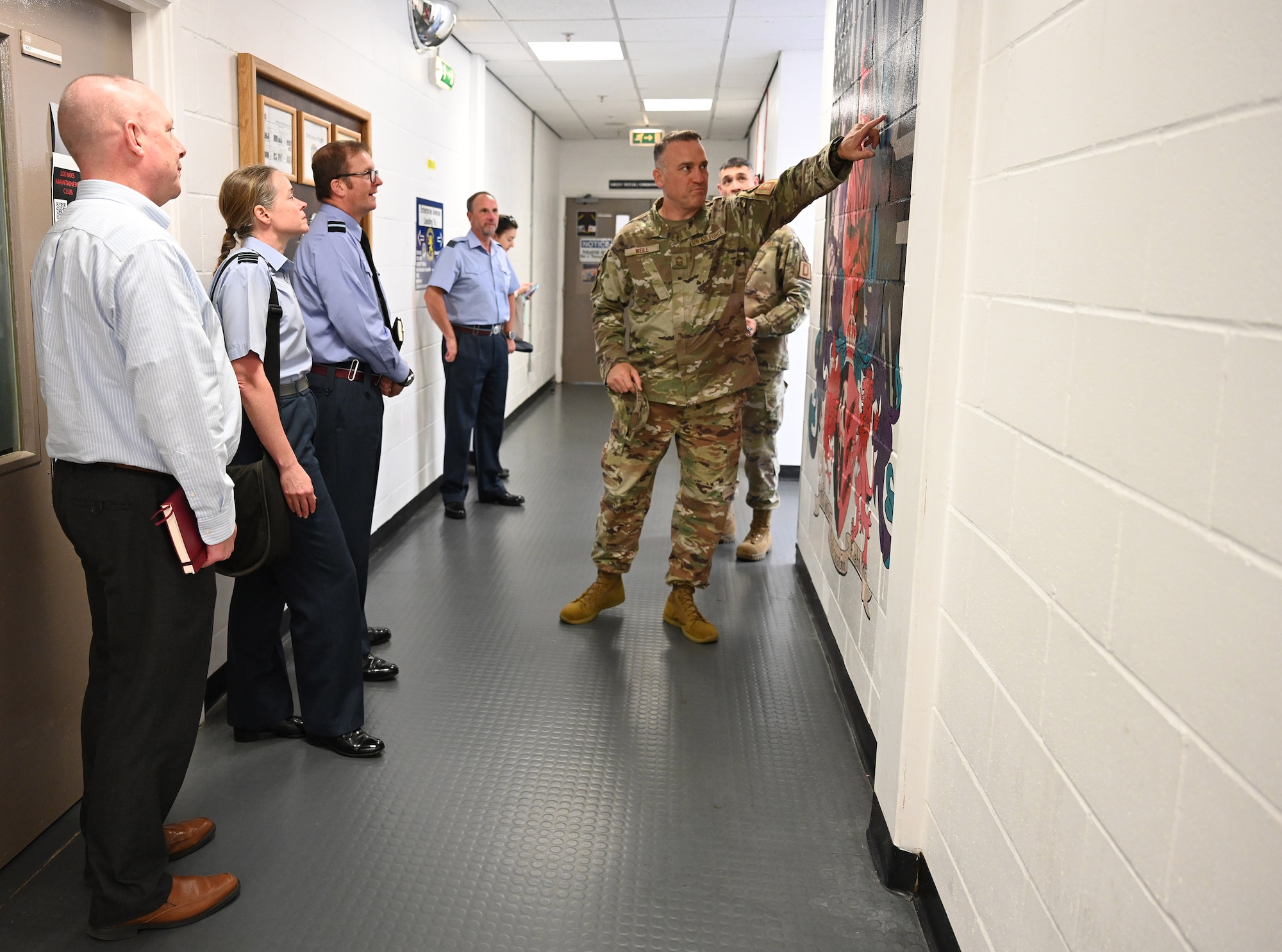 U.S. Air Force Chief Master Sgt. Jason Weill, right, 100th Maintenance Group senior enlisted leader, shows off a mural – painted by 100th MXG Airmen – to Air Commodore Simon Strasdin, third left, Royal Air Force Intelligence, Surveillance, Target Acquisition and Reconnaissance force commander, based at RAF Waddington, and Wing Commander Sal Berris, second left, ISTAR SO1 Rivet Joint Program, during a visit to RAF Mildenhall, England, Aug. 23, 2023. Strasdin was here to strengthen United Kingdom-US relationships and thank 100th ARW, 95th Reconnaissance Squadron and 488th Intelligence Squadron Airmen for their hard work and cooperation in the joint partnership program between the RAF and U.S. Air Force reconnaissance aircraft. (U.S. Air Force photo by Karen Abeyasekere)