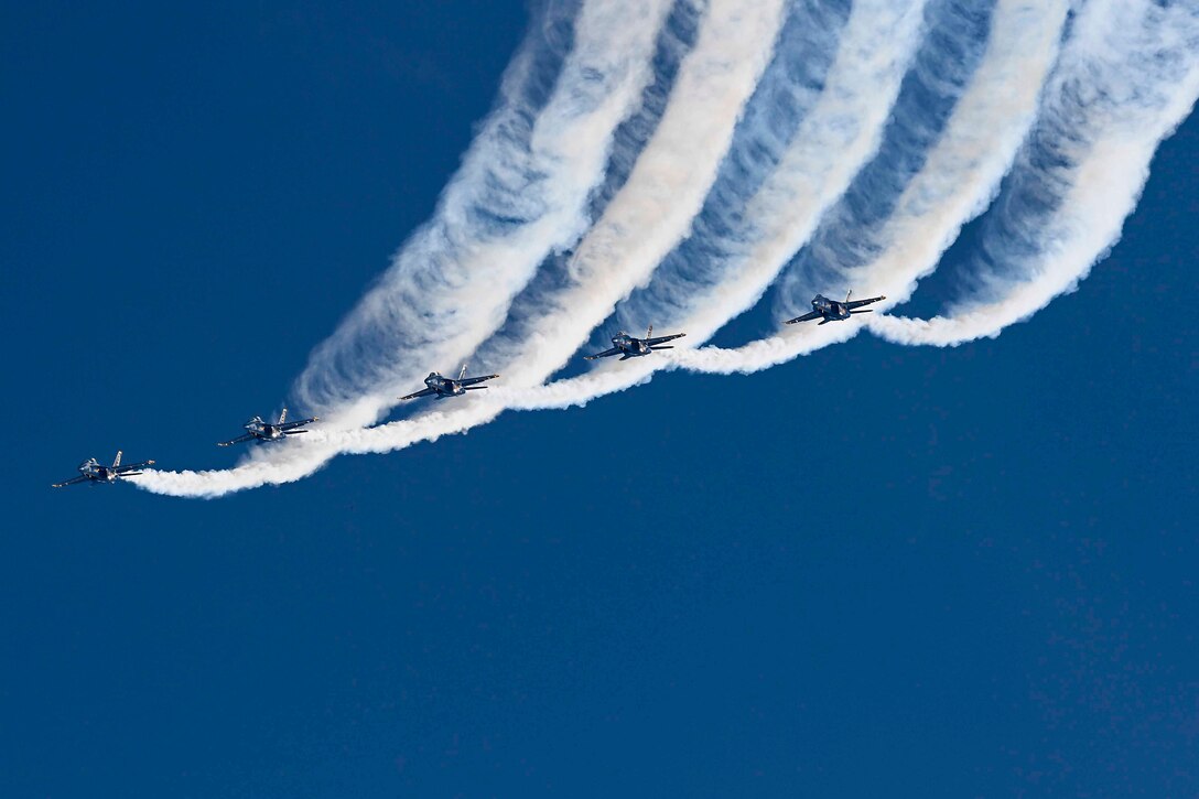 Five aircraft fly in formation as jet streams trail behind them.