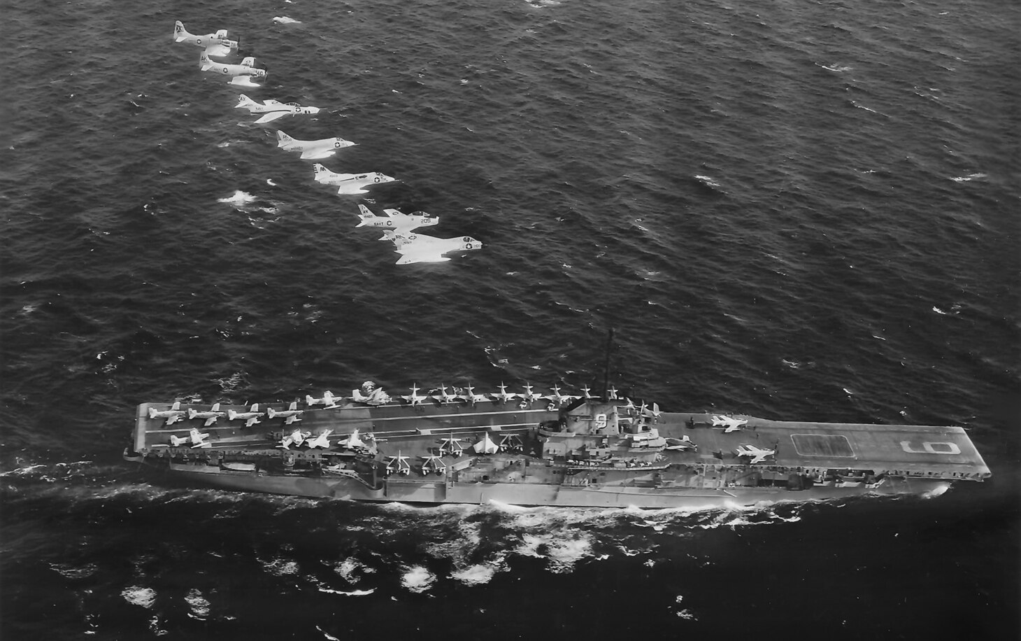 The class lead ship, USS Essex (CV 9), with aircraft of Carrier Air Wing (CVW) 10 on the flight deck and in the air, including AD Skyraiders, and new jets, F4D Skyrays, A4D Skyhawks, FJ Furys and F9F Cougars.