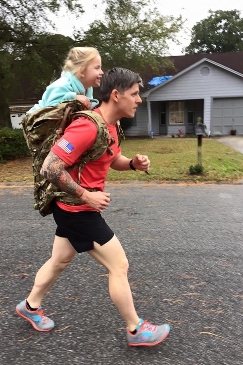 A person power walks through a street with a child on their shoulders.