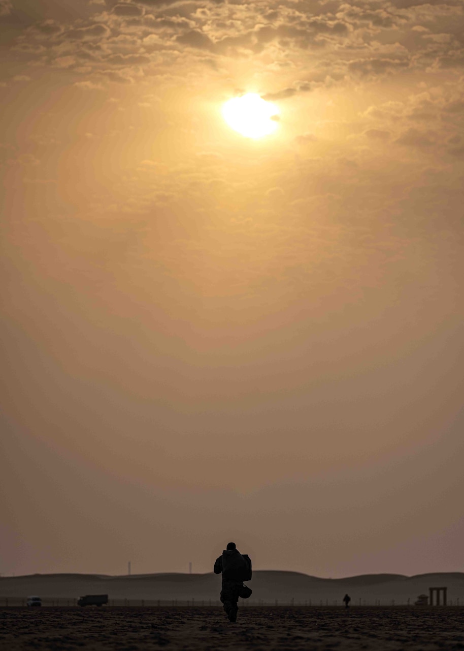 A soldier shown in silhouette walks under the sun.