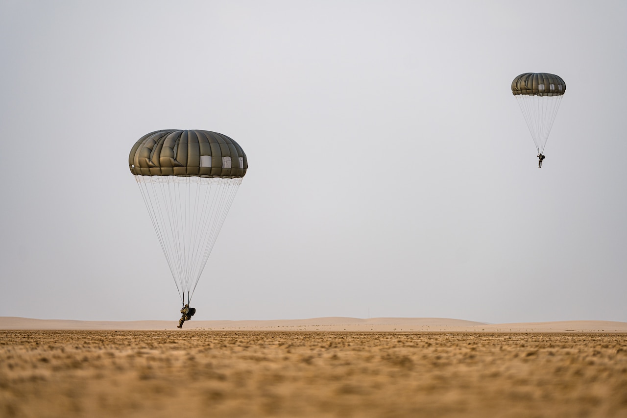 Two soldiers descend in the sky wearing parachutes.