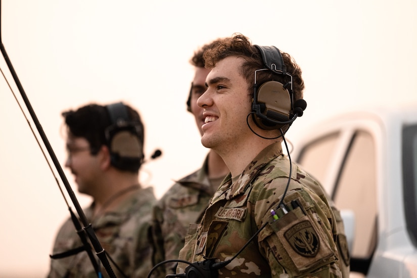 Three airmen stand as a group wearing headsets.