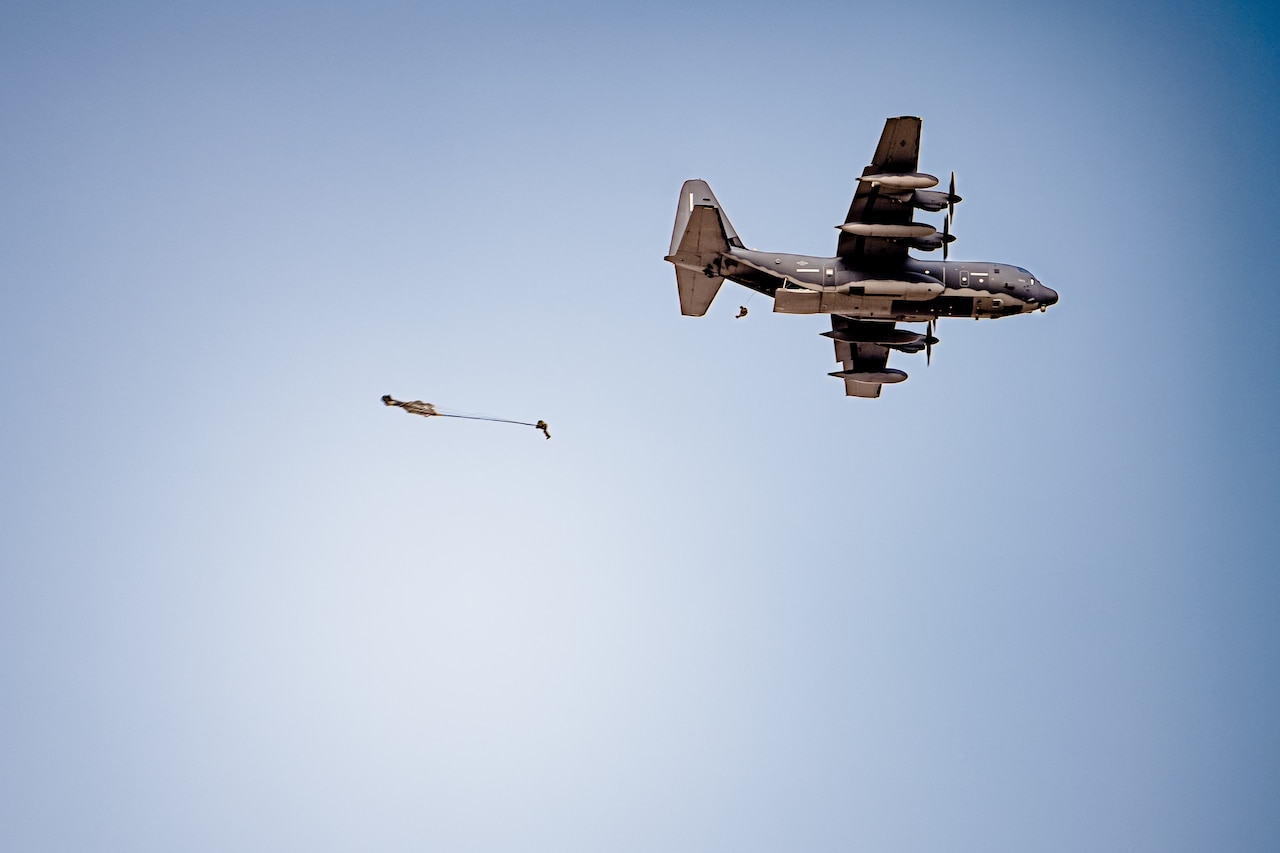 A soldier descends in the sky wearing a parachute underneath an airborne aircraft.