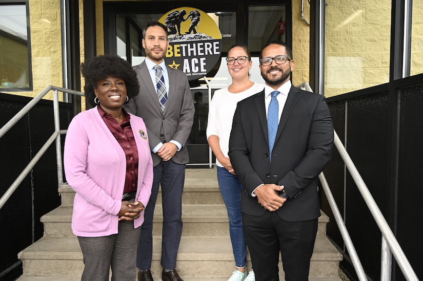 Four people pose on stairs leading up to a door with a sign in front of it.