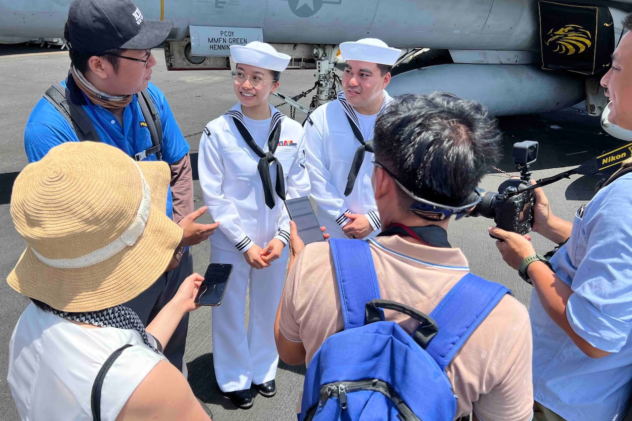 Two sailors speak to a group of people.
